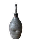 A beige, gray, and brown ceramic oil cruet with a spout and black accents on a white background.