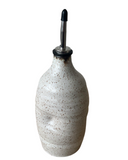 A beige, gray, and brown ceramic oil cruet with a spout and black accents on a white background.