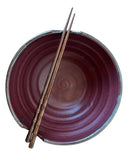 Purple ceramic bowl with a pair of wooden chopsticks on a white background
