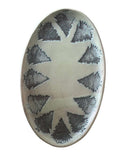 An oval ceramic plate with a textured, matte avocado glaze and a repeating pattern of dark bronze stylized pine trees arranged around a central star shape, shown on a plain soft green background.