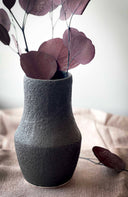 Textured gray vase with purple leaves on a neutral background