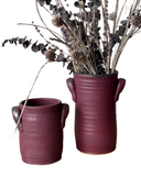 Two Luna Utensil Holders, one small holding a wine bottle and the other large with wooden utensils, both in a beige color with stamped handles.