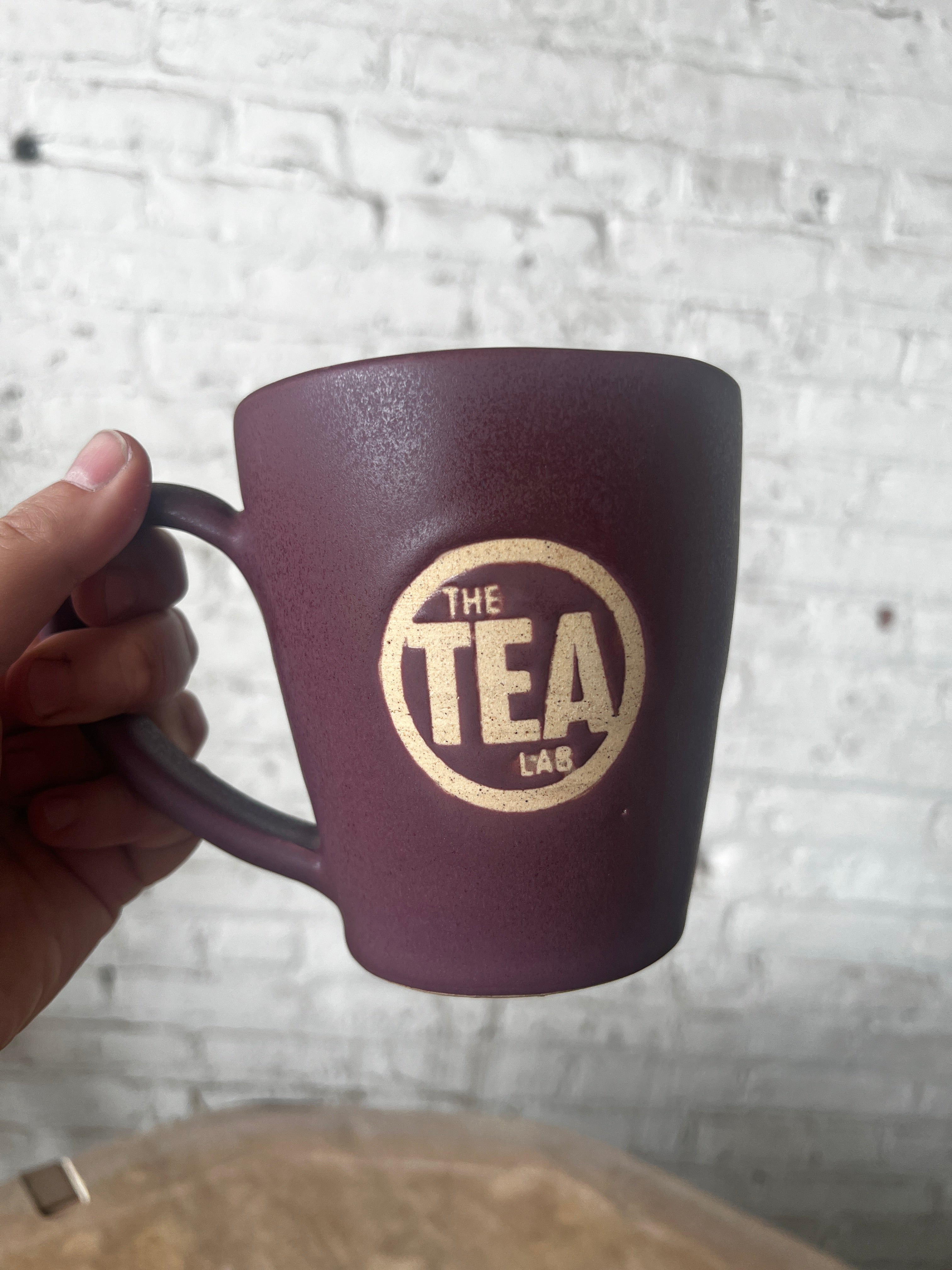 Purple mug with 'The Tea Lab' logo held by a hand against a textured white background
