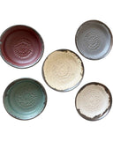 Five ceramic plates in various colors with textured designs on a white background