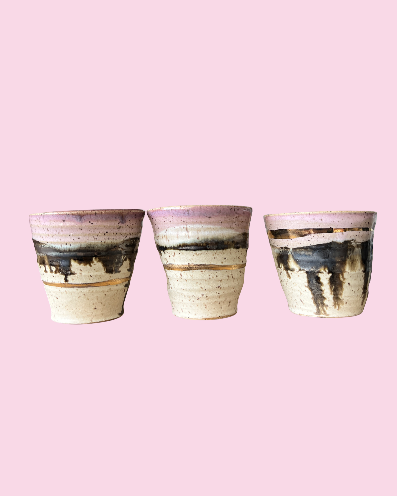 Three ceramic pots with a rustic finish on a pink background