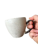 Hand holding a speckled ceramic mug against a white background