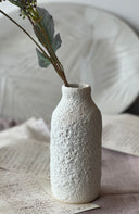 Textured ceramic vase with a plant on a surface with paper