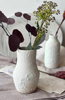 White textured vase with flowers on a surface with a blurred background
