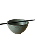 Ceramic bowl with a textured surface and black chopsticks on a white background