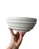 Beige bowl on a white background being held by a hand. 
