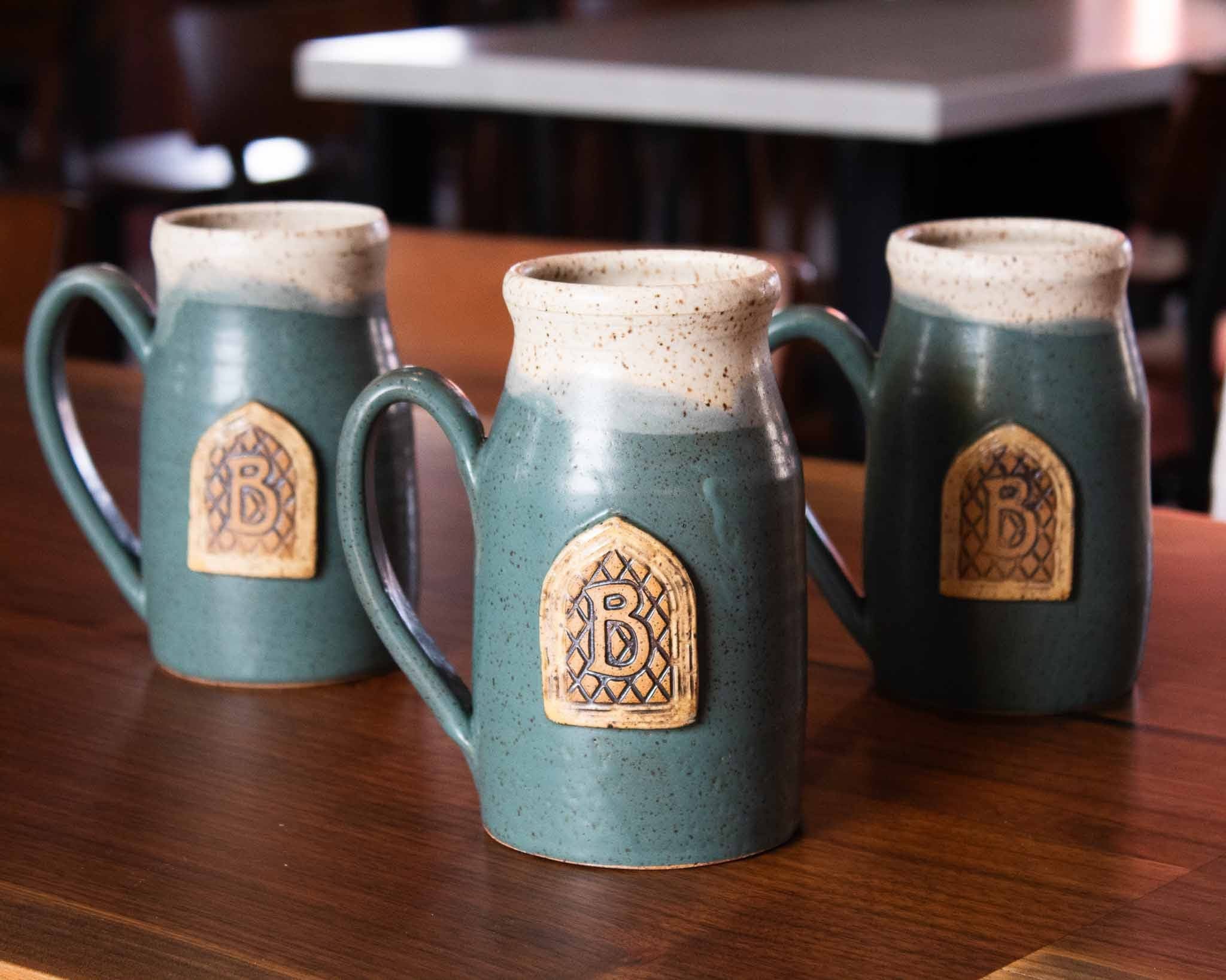 Three ceramic mugs with decorative logos on a wooden table.