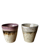 Two ceramic cups with speckled glaze on a white background