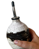 Hand holding a ceramic oil dispenser with a black and white speckled design on a white background