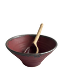A beige ceramic bowl with a black rim, accompanied by a wooden spoon.
