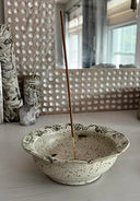 Ceramic incense burner with a single stick of incense on a light surface.