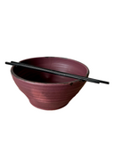 A set of handcrafted ceramic bowls in various colors, with a rustic texture, stacked together with a pair of chopsticks resting on top.