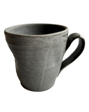 A handmade ceramic mug with a textured, speckled gray exterior and a dark, glossy black interior and handle, shown on a plain white background.