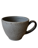 A beige speckled stoneware cappuccino mug with a bronze accented handle and matte glaze.