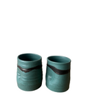 Two teal ceramic cups with black stripes on a white background