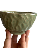 Hand holding a green ceramic bowl against a white background