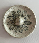 Speckled ceramic plate with leaf patterns on a white background