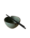 Green ceramic bowl with black interior and two black chopsticks on a white background