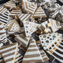 A pile of ceramic Christmas tree ornaments in various designs, featuring white, brown, and gold patterns including stripes, polka dots, and metallic gold leaf accents.