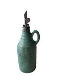 A teal handmade olive oil bottle with a gunmetal and black weighted pouring spout on a white background. 