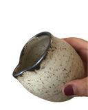 Hand holding a ceramic cup with speckled design on a white background