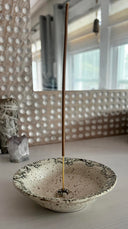 Incense stick in a decorative ceramic bowl with a textured wall in the background