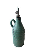 A teal handmade olive oil bottle with a gunmetal and black weighted pouring spout on a white background. 