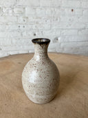 Speckled ceramic vase on a wooden surface with a white brick wall background