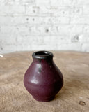 Small brown ceramic vase on a textured surface with a light gray background