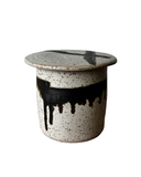 A collection of four Luna French Butter Crocks in various colors, from left to right: beige with dark speckles, gray with bronze highlights, blue with bronze highlights, and purple with bronze highlights. Each crock has a small protrusion on the top and is approximately 3.