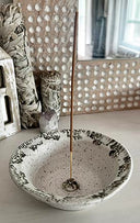 Ceramic bowl with incense stick on a light surface, decorative wall in the background