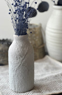 Textured white vase with dried flowers on a textured surface