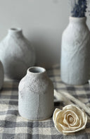 Set of gray ceramic vases on a checkered tablecloth with a white flower.