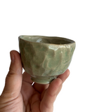 Hand holding a green ceramic cup against a white background