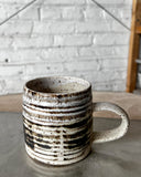 Speckled ceramic mug on a concrete surface with a textured wall background