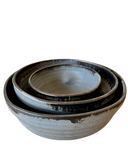 A set of three beige ceramic nesting bowls with rustic finishes and organic shapes, stacked together.