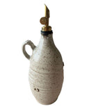 A beige and bronze handmade olive oil bottle with a gold weighted pouring spout on a white background. 