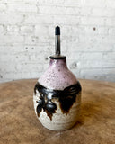 Ceramic oil dispenser with black speckles on a wooden surface and white brick wall background