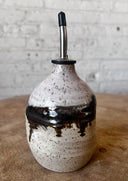 Speckled ceramic oil dispenser with black accents on a wooden surface.