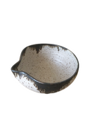 A hand holding a small, beige and brown ceramic pouring bowl with a spout.
