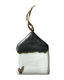A ceramic house-shaped ornament with a bronze roof and white body, hanging from a twine.