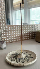 Incense stick on a decorative stone holder with a textured wall and mirror in the background