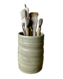 Ceramic cup with textured surface holding various paintbrushes on a white background