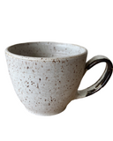 A beige speckled stoneware cappuccino mug with a bronze accented handle and matte glaze.