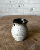 Speckled ceramic vase on a textured surface with a neutral background