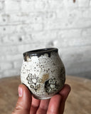 Hand holding a small ceramic cup with floral designs against a textured wall background